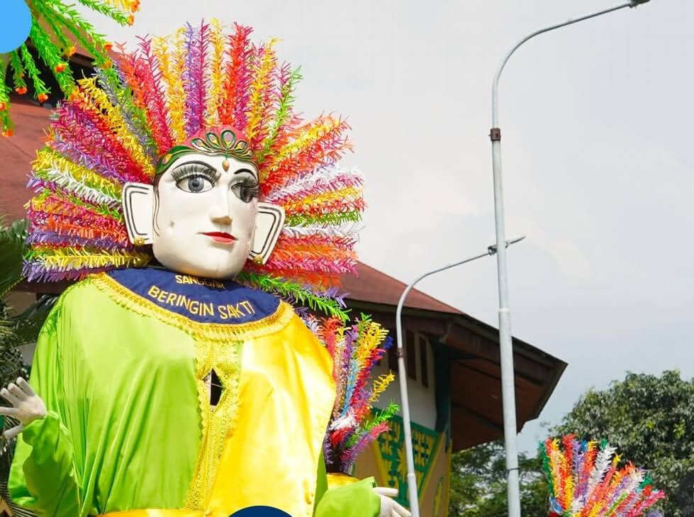 Festival float with a large mask like head wearing a bright neon green and yellow robe and a rainbow spiky headdress